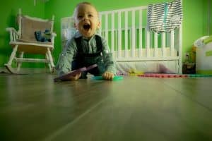 laughing toddler on wooden floor- white cot-white chair-some toys