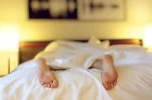 Person lying in bed face down -covered by blanket except feet