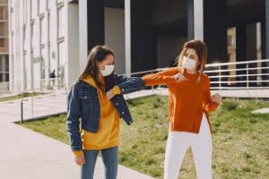 young women in medical masks greeting each other with the elbow