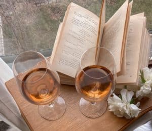 Open book with 2 glasses of wine on a wooden table by a window